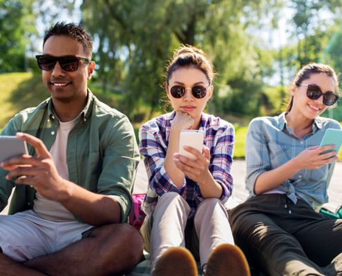 Young adults using mobile devices or apps in the summer sun.