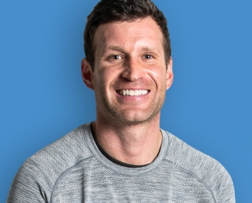 Headshot of Brandon Slade in grey shirt on blue background.