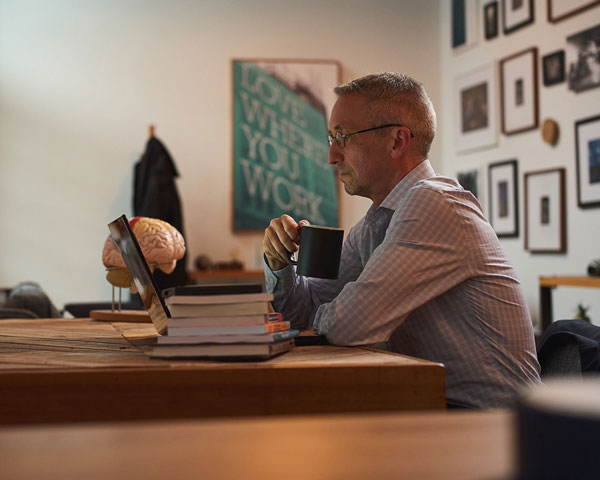 Dr. Russell Ramsay is in his office holding a coffee mug and looking at a laptop.