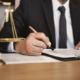 A lawyer signing a contract next to a scale on a table.