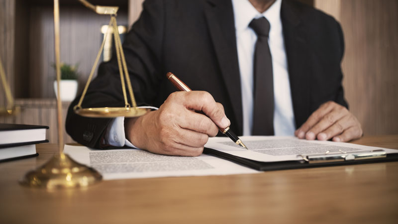 A lawyer signing a contract next to a scale on a table.